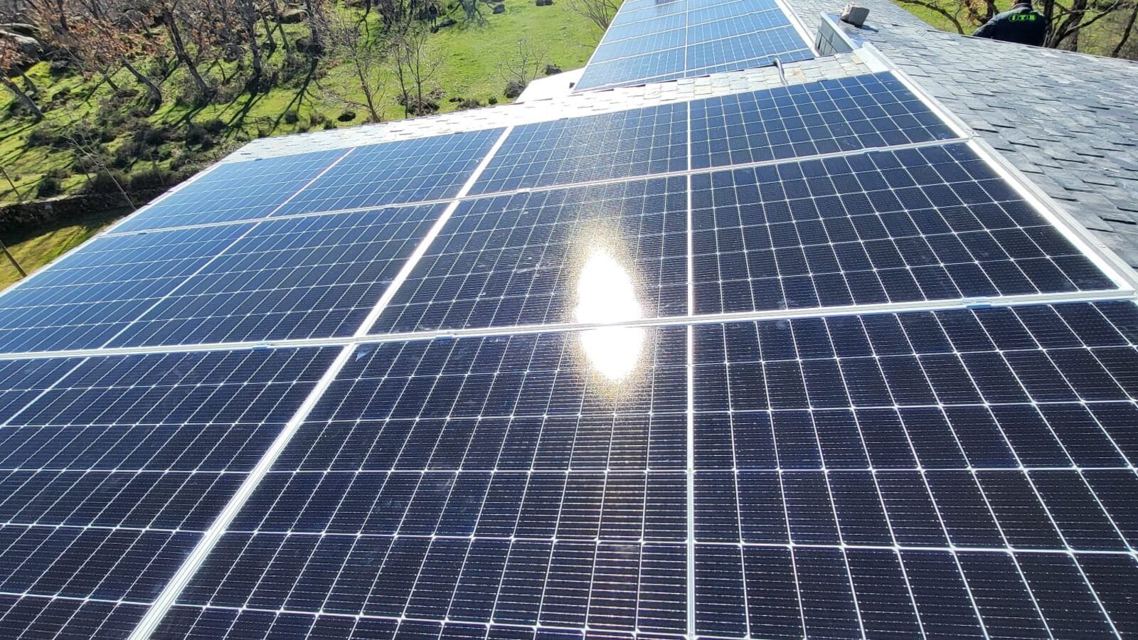 Módulos fotovoltaicos sobre la cubierta de pizarra de una vivienda, con la sierra al fondo